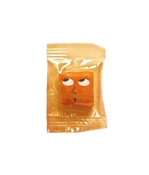 A small orange square item sealed in a shiny translucent gold wrapper, with a simple face printed on the front, shown on a plain light background.