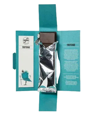 A packaged chocolate bar presented in an open teal paper sleeve with printed text panels on both sides. The chocolate is wrapped in reflective silver foil, and the brand name 'TRITONE' is visible on the left panel.